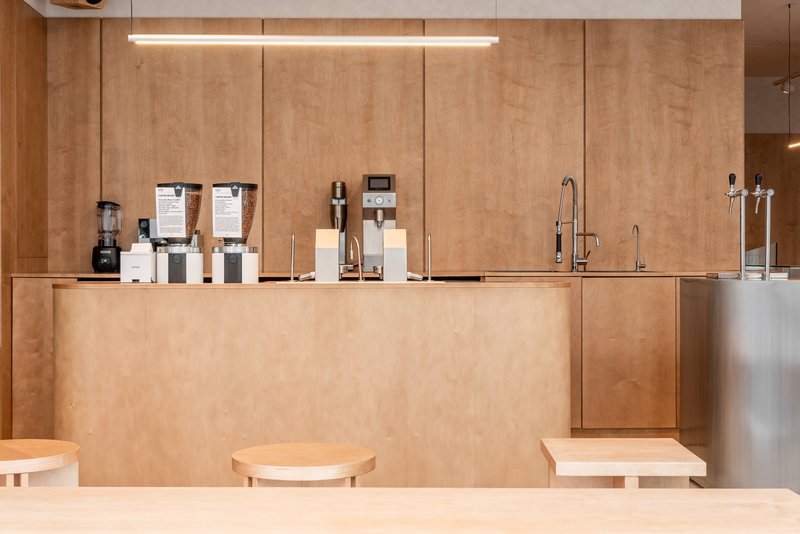 Service counter in plywood with coffee equipment and tap fixtures under linear ceiling lights