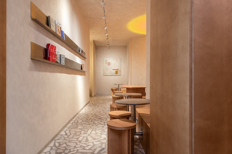 Narrow corridor with terrazzo flooring leading to a framed artwork under warm track lighting