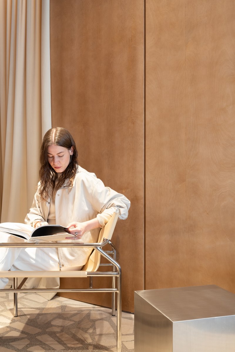 Woman reading at a tubular metal lounge chair against floor-to-ceiling plywood paneling