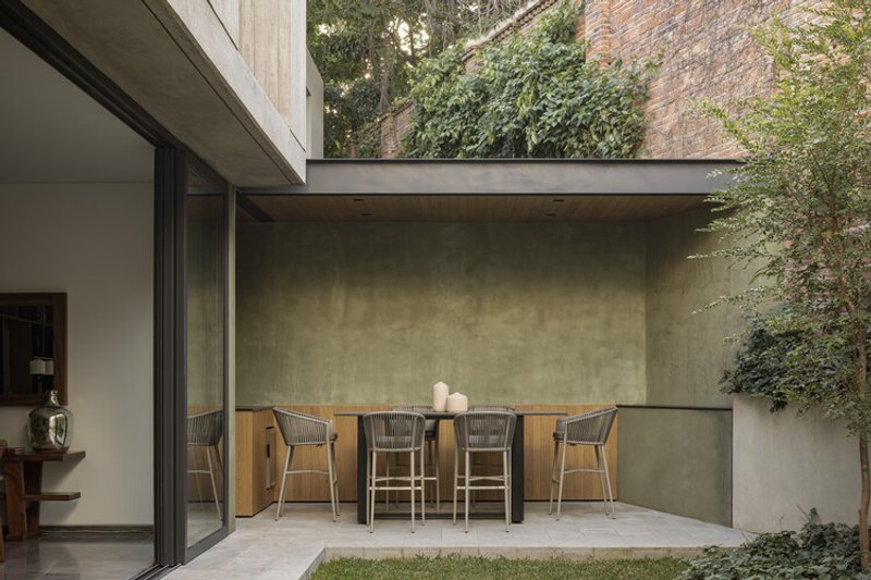 Covered outdoor dining terrace with polished concrete ceiling and planted brick walls beyond