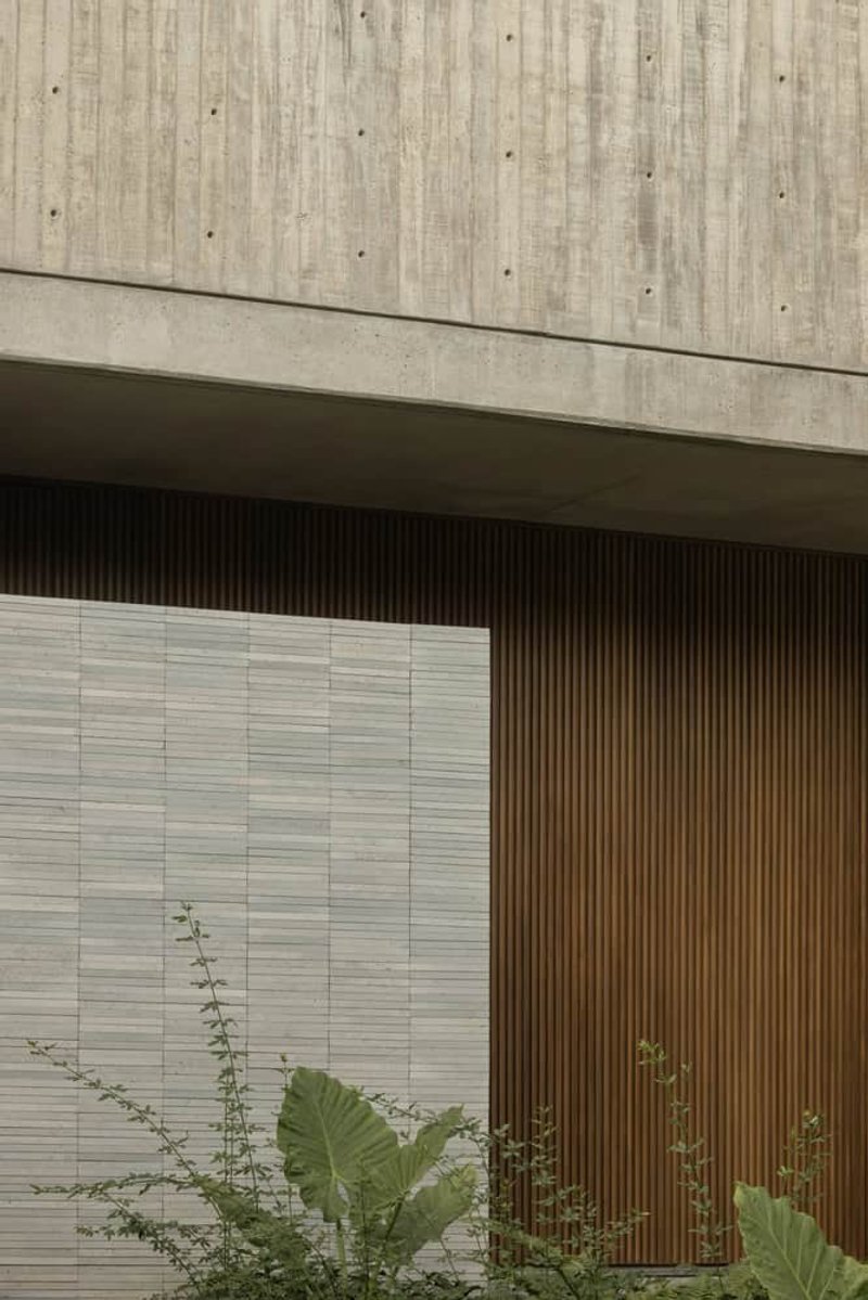 Board-formed concrete canopy above a travertine tile wall and vertical timber screen with tropical plantings