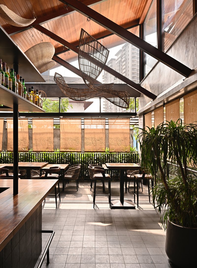 Dining space under a pitched timber ceiling with exposed steel trusses and woven basket chandeliers suspended overhead
