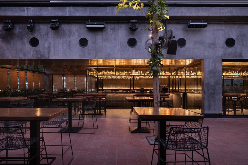 Courtyard view at night showing backlit bar with copper canopy and concrete columns with circular voids