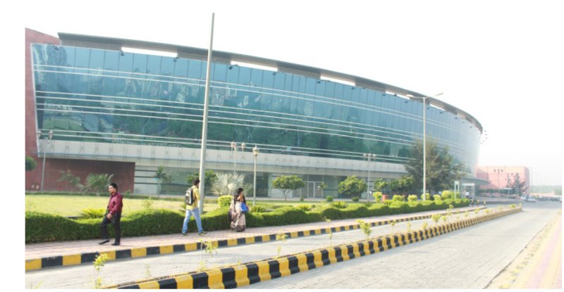 Curved glass facade at street level with pedestrians walking along the planted median