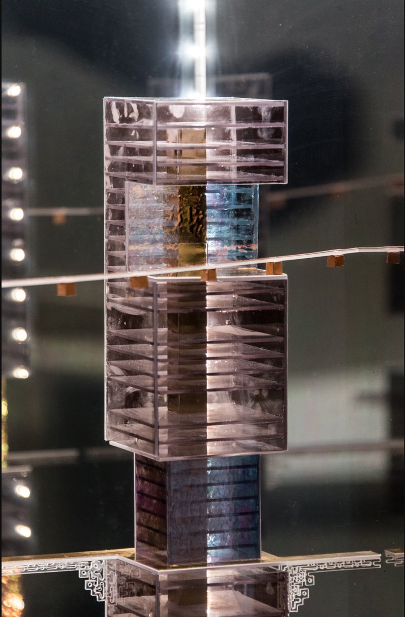 Stacked transparent model components with layered horizontal louvers and colored central cores under gallery lighting