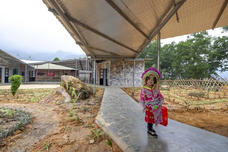 Concrete walkway beneath a corrugated roof canopy with a child walking alongside a planted bed