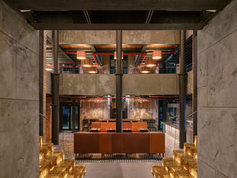 Symmetrical entry corridor framed by concrete pilasters with backlit recessed floor panels in amber glass