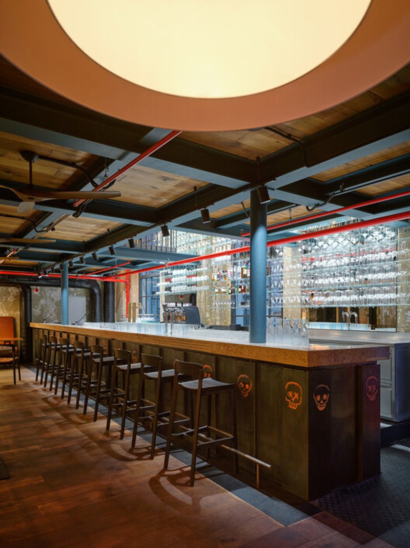Long bar counter with timber base panels and a glass display wall under timber ceiling beams