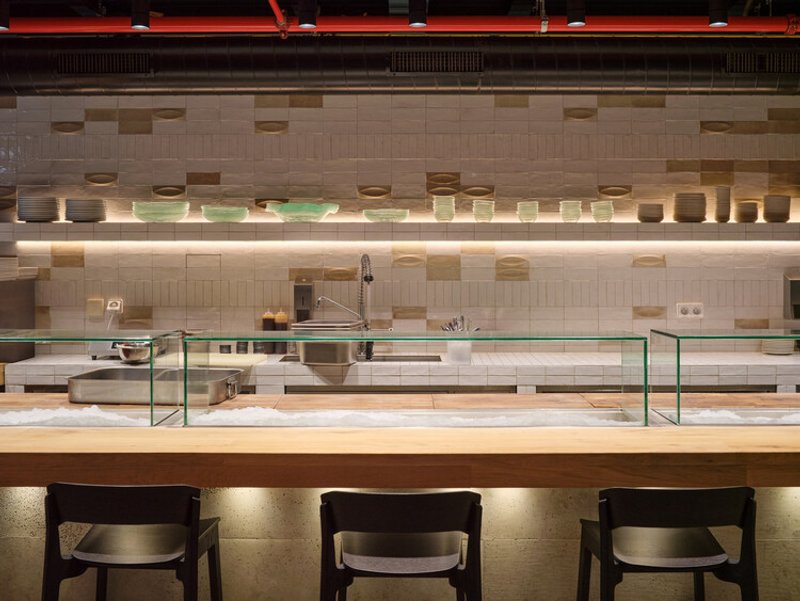 Kitchen counter with glass sneeze guards below a tiled wall with integrated strip lighting