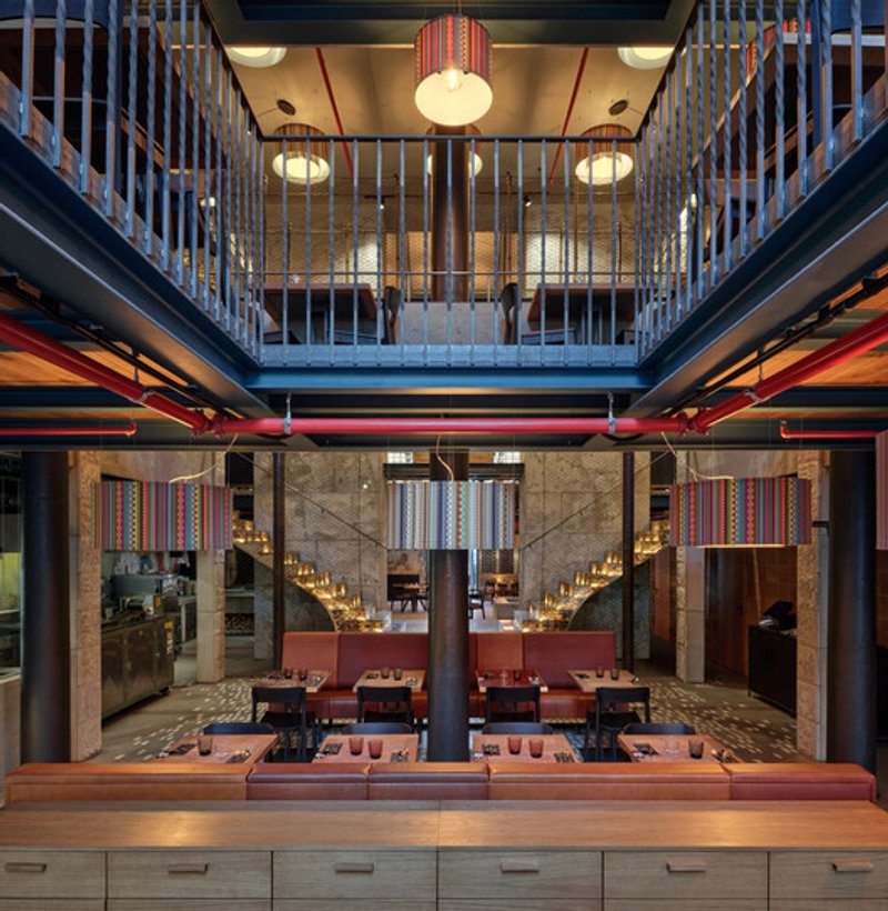 Double-height dining hall with central column, mezzanine railings, and exposed red conduit pipes