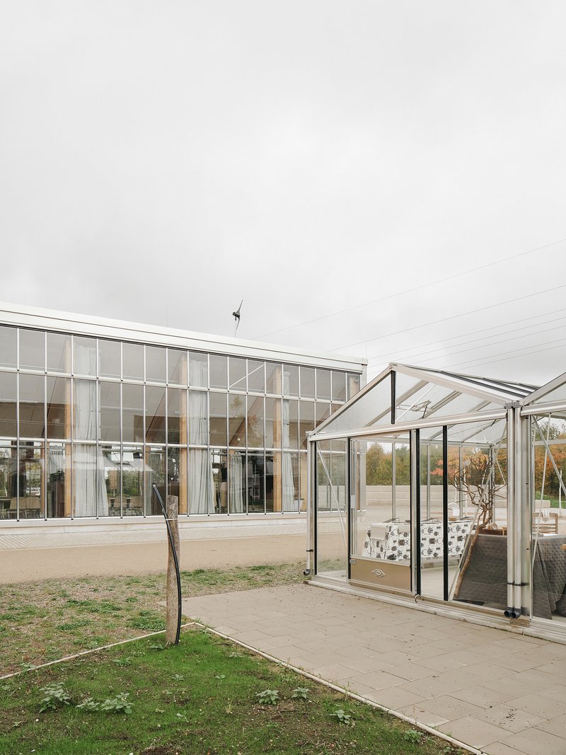 Glazed long facade with an adjacent small greenhouse and a wind turbine on the ridge