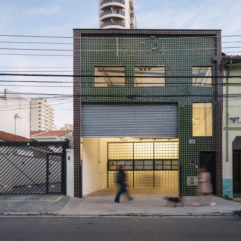 Street facade with glass block tiles and green metal frames as pedestrians pass at dusk