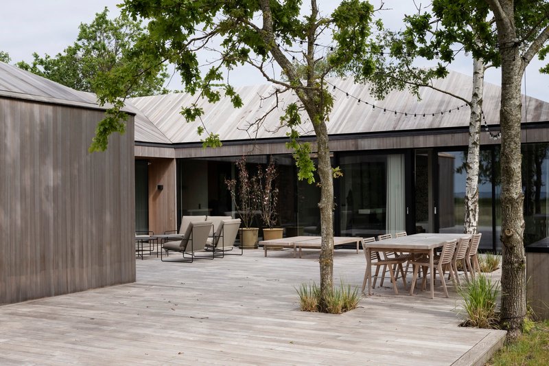 Timber deck courtyard with outdoor dining furniture and lounge chairs beneath overhanging tree branches and string lights