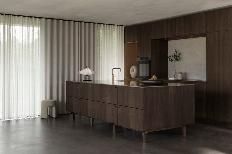 Kitchen island with dark wood cabinetry and polished concrete floor illuminated by sheer curtains filtering daylight
