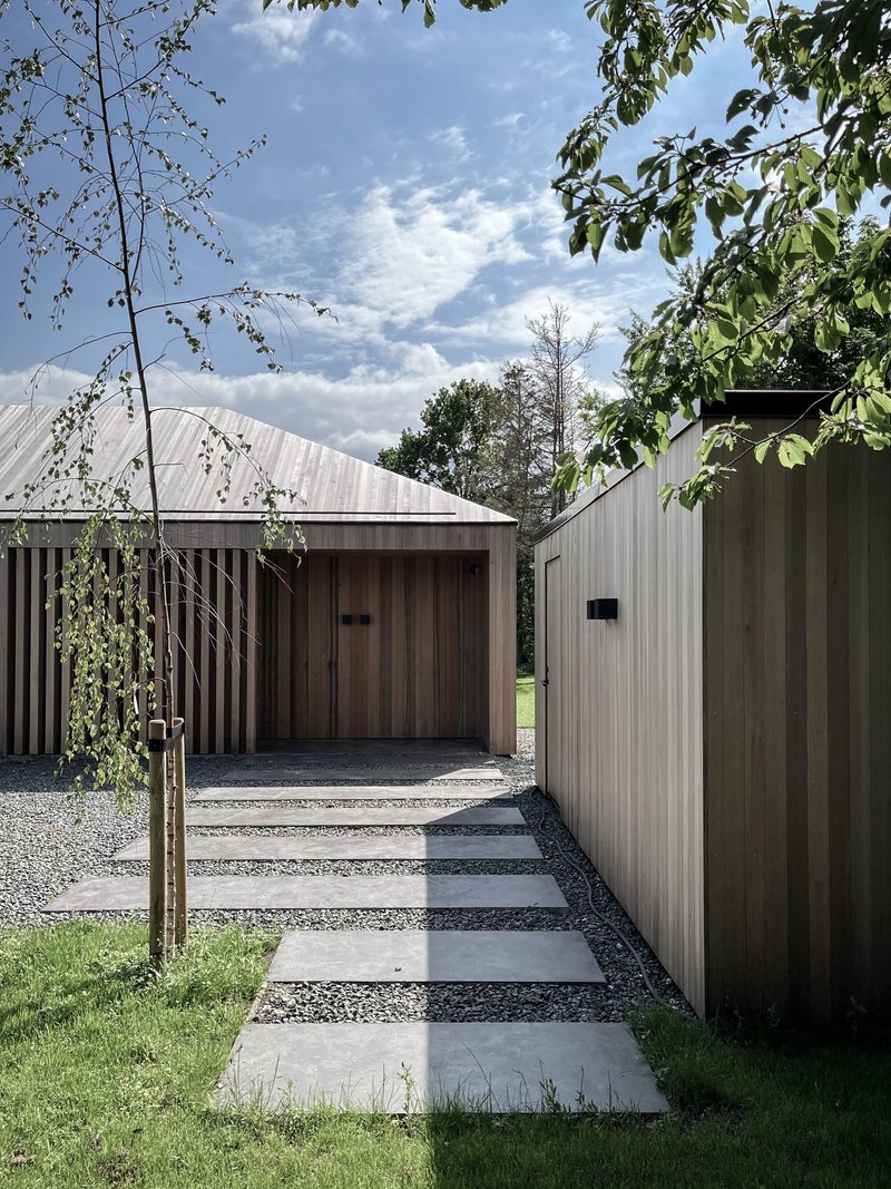 Entrance pathway with stepping stones through gravel flanked by vertical timber cladding under cloudy skies