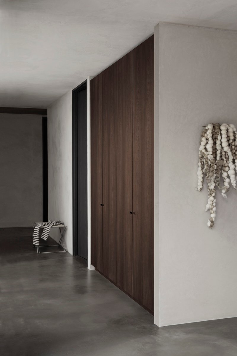 Floor-to-ceiling timber storage wall with recessed handles along a polished concrete hallway