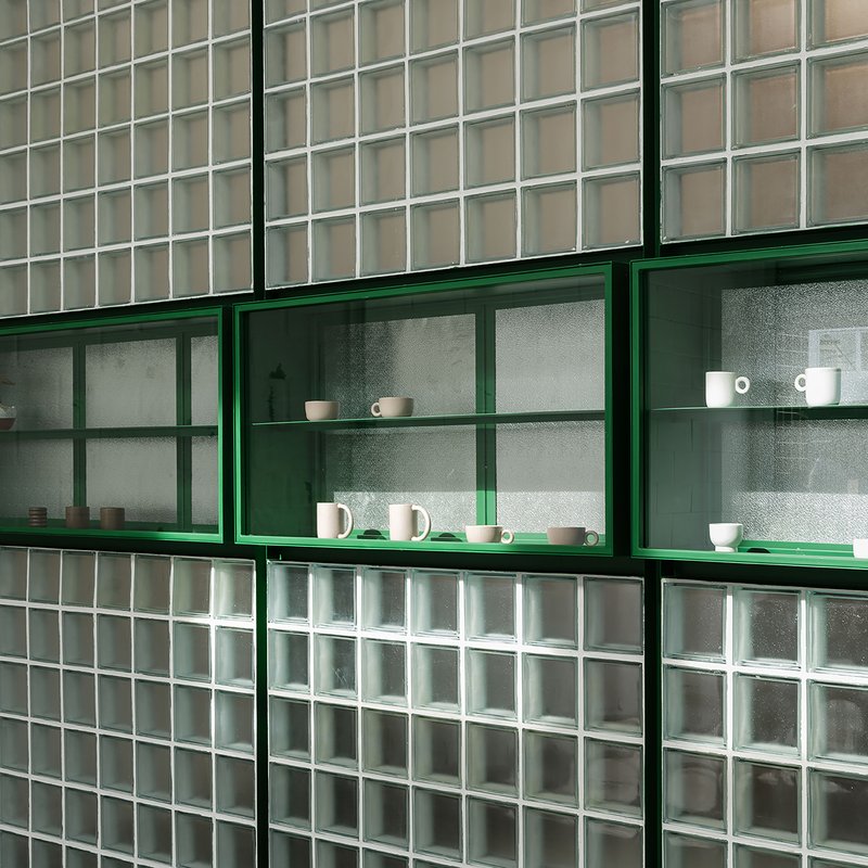 Green metal shelving with frosted glass backing set within translucent glass block wall
