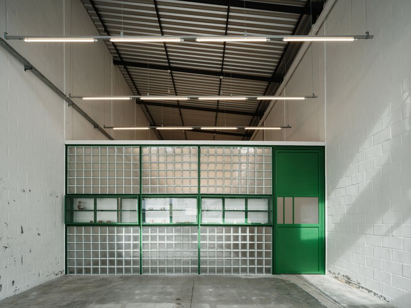 Interior view of green-framed glass block facade with corrugated metal ceiling and linear fluorescent fixtures