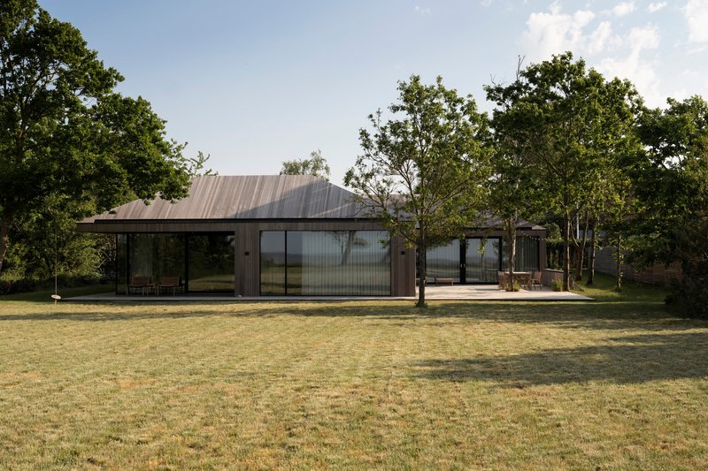 Long view of the single-story residence with corrugated metal roof and glass walls set among trees in dry grass