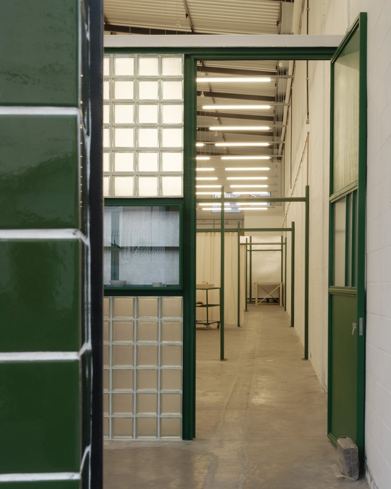 View through green steel framed doorway showing glass block wall and exposed linear ceiling lights above corridor