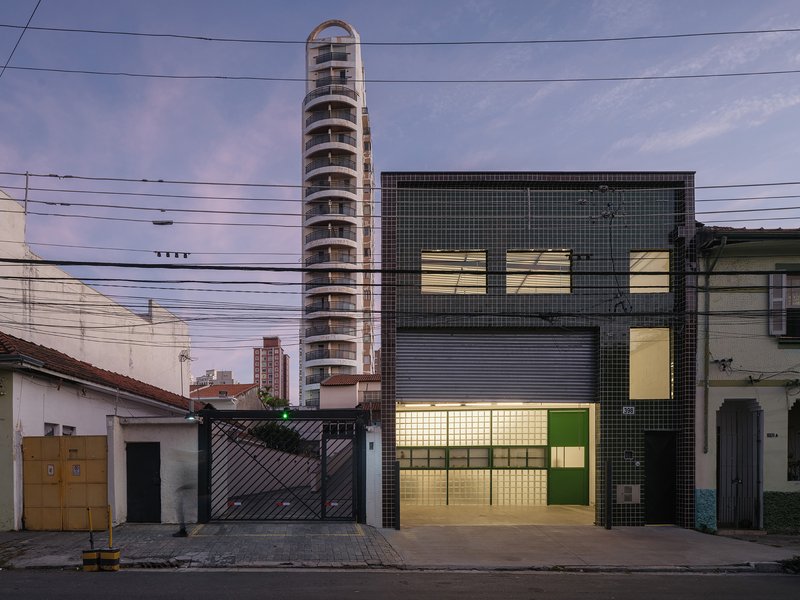 Evening view of illuminated facade with glass block and green tile next to neighboring tower under purple sky