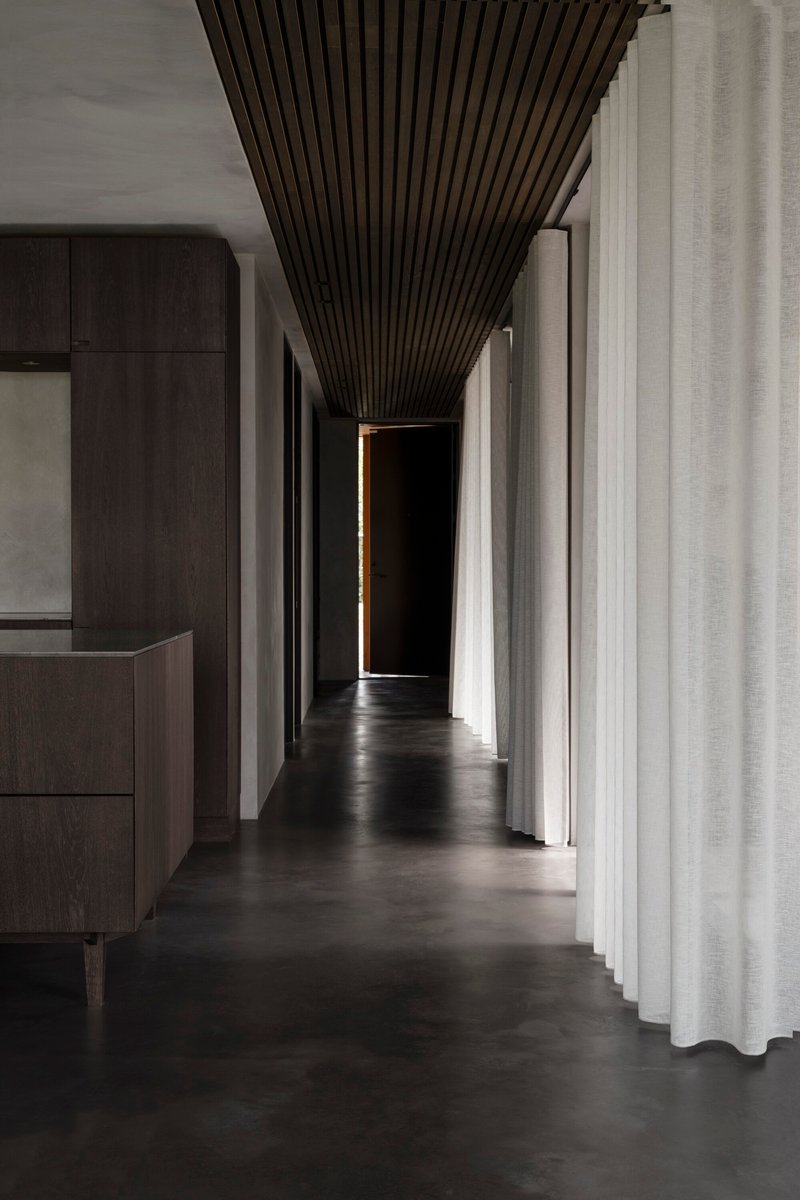 Corridor with dark slatted ceiling tapering toward a doorway illuminated by a narrow strip of light