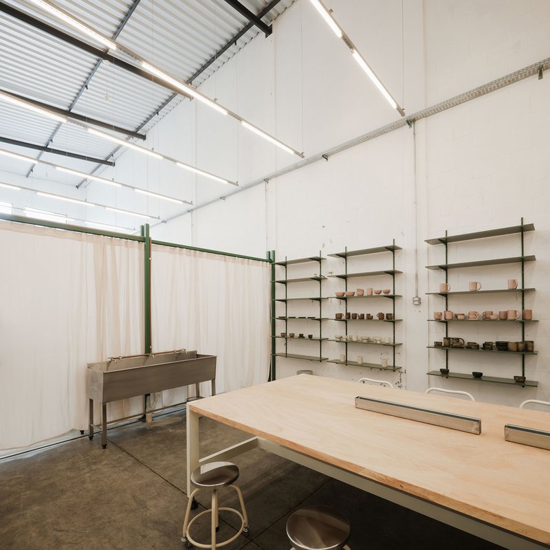 Workshop interior with plywood work table, green shelving, sheer curtain partition, and corrugated metal ceiling