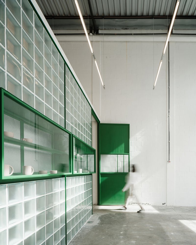 Interior corridor with translucent glass block wall framed in green steel under linear ceiling lights