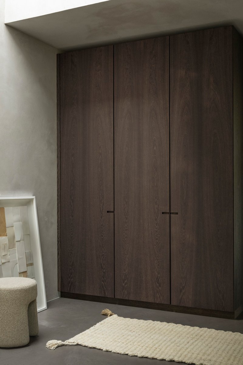 Floor-to-ceiling dark oak wardrobe with minimal black handle detail against pale plaster walls
