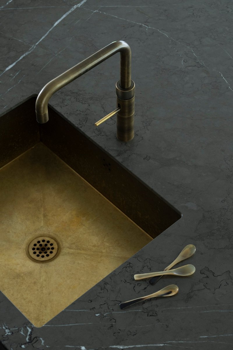 Brass sink faucet and undermount basin set into dark marble countertop with veining