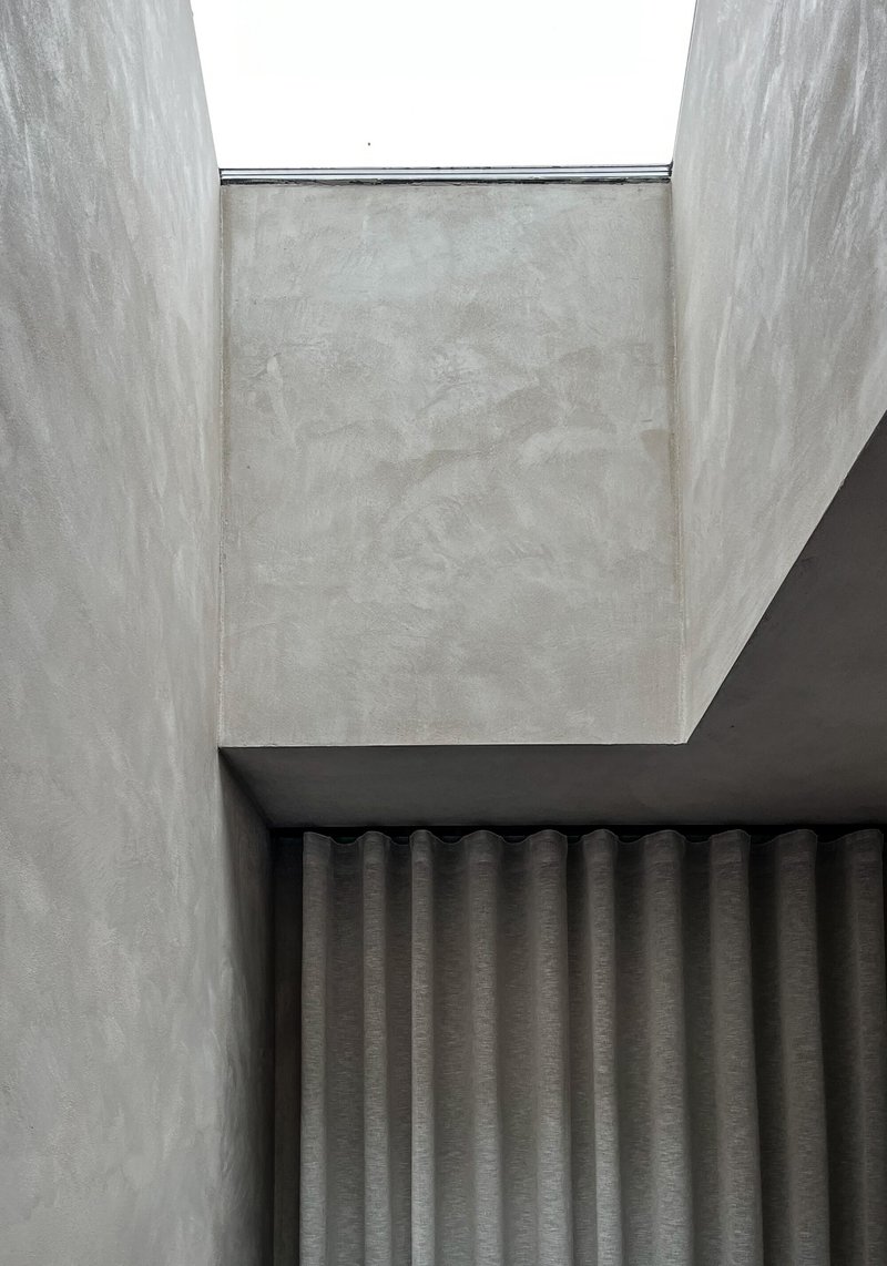 Concrete skylight shaft with narrow clerestory window above pleated grey curtain