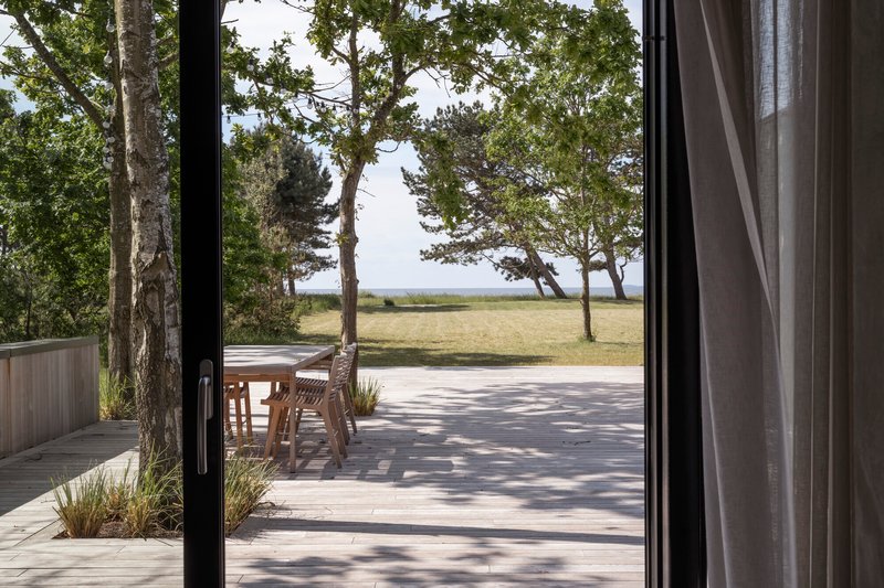 Timber deck framed by black sliding doors opening to lawn and coastal trees