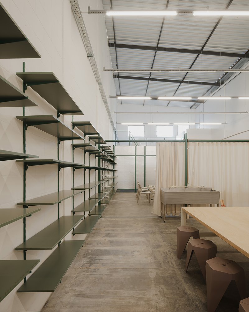Long corridor lined with green metal shelving and plywood workbenches on polished concrete floor