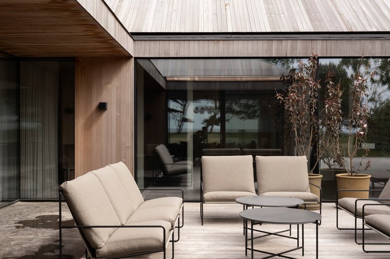 Terrace with timber-clad volumes and floor-to-ceiling glazing framed by upholstered lounge furniture and potted plants