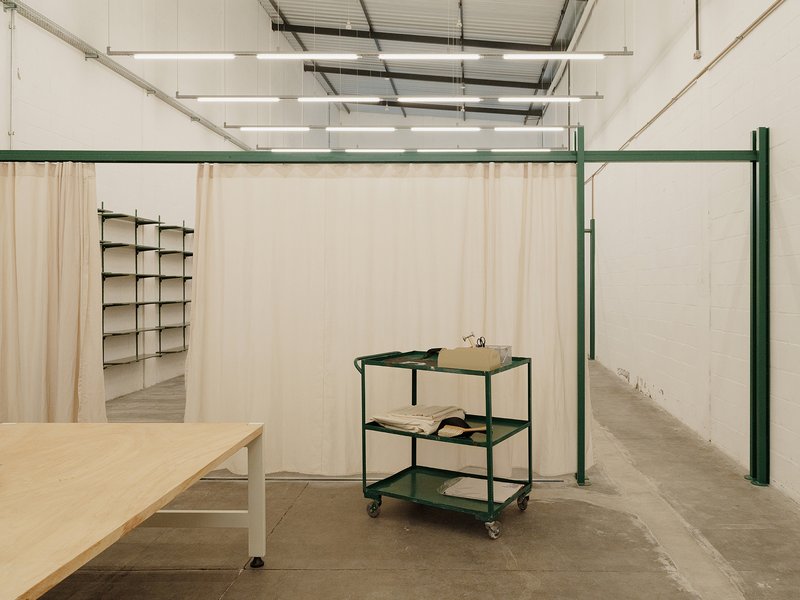 Green steel framing system with fabric panels dividing the workspace and a three-tier rolling cart