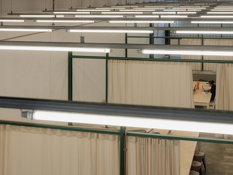 Elevated view across multiple fabric-partitioned workspaces with green steel frames and fluorescent lighting