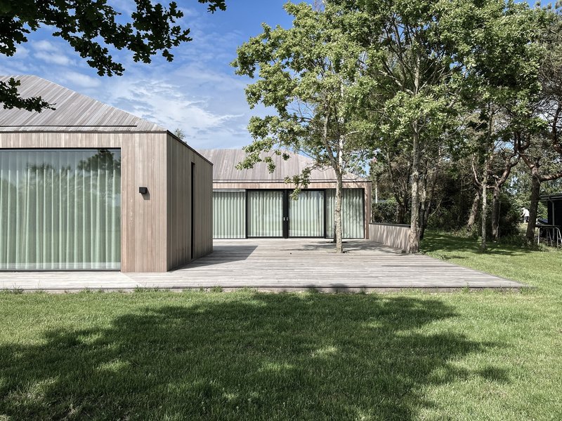 Gabled volume clad in vertical timber and corrugated metal viewed across mown lawn on a sunny day