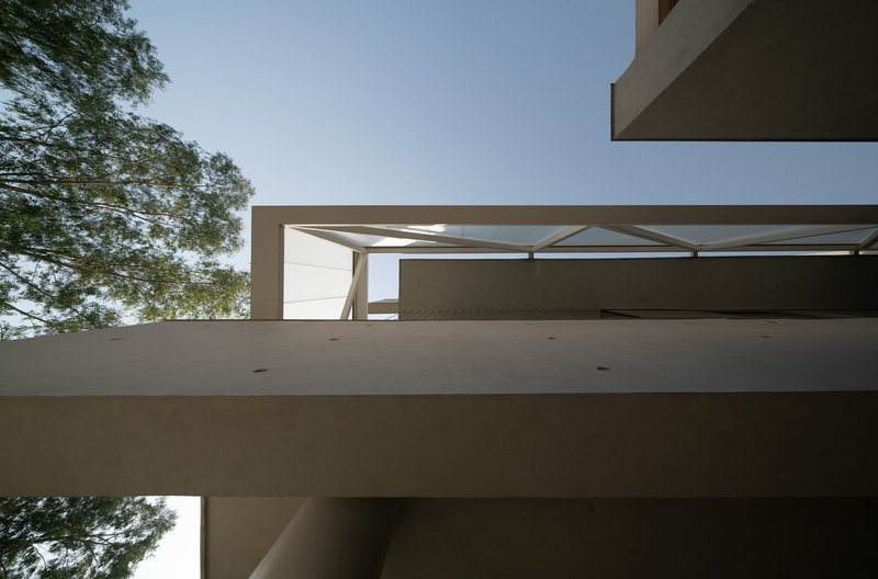 Upward view of layered balconies with diagonal tensile bracing and tree canopy framing the composition