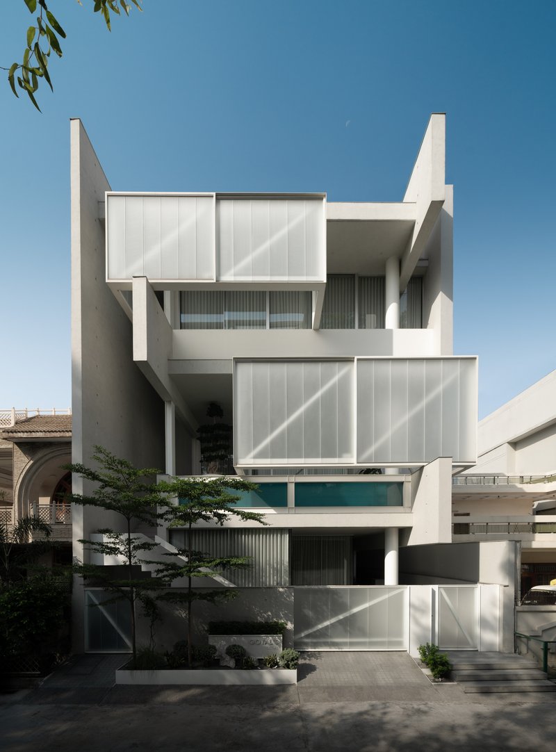 Street facade with stacked white volumes, diagonal-paneled screens, and a small tree in the forecourt