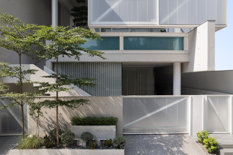 Entry courtyard with planted concrete beds, young trees, and vertical louvered screening in morning light
