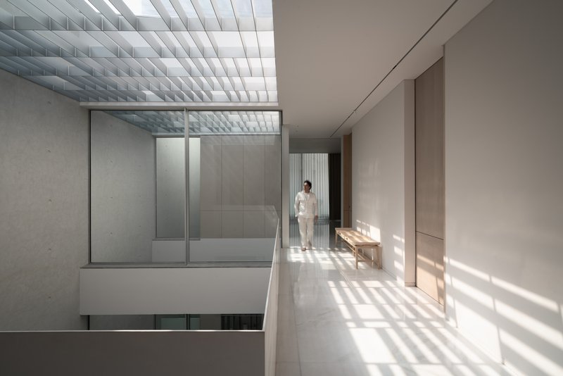 Upper corridor with baffled skylight casting striped shadows on white terrazzo flooring