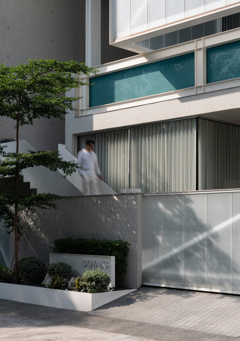 Ground level entrance showing white metal louvered screens with planted beds and a figure ascending the staircase