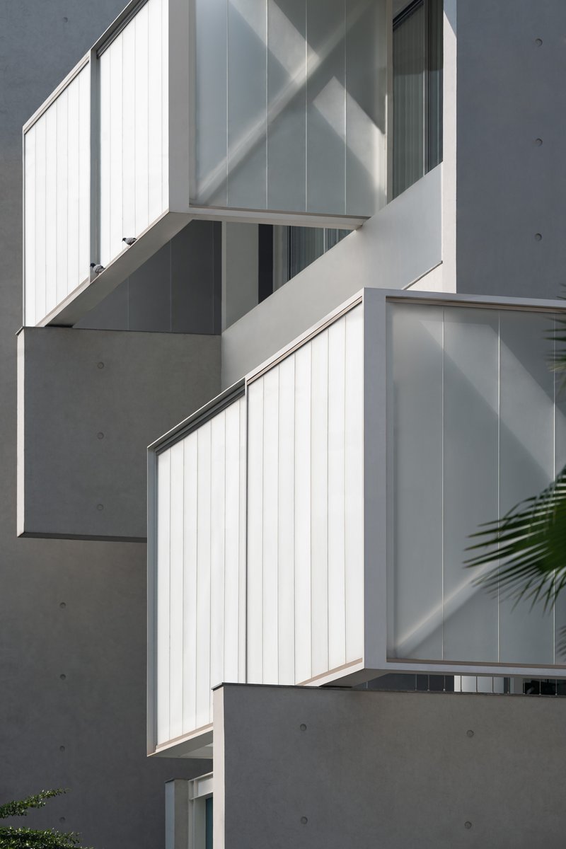 Stacked balconies with white vertical cladding panels and exposed concrete walls in afternoon light