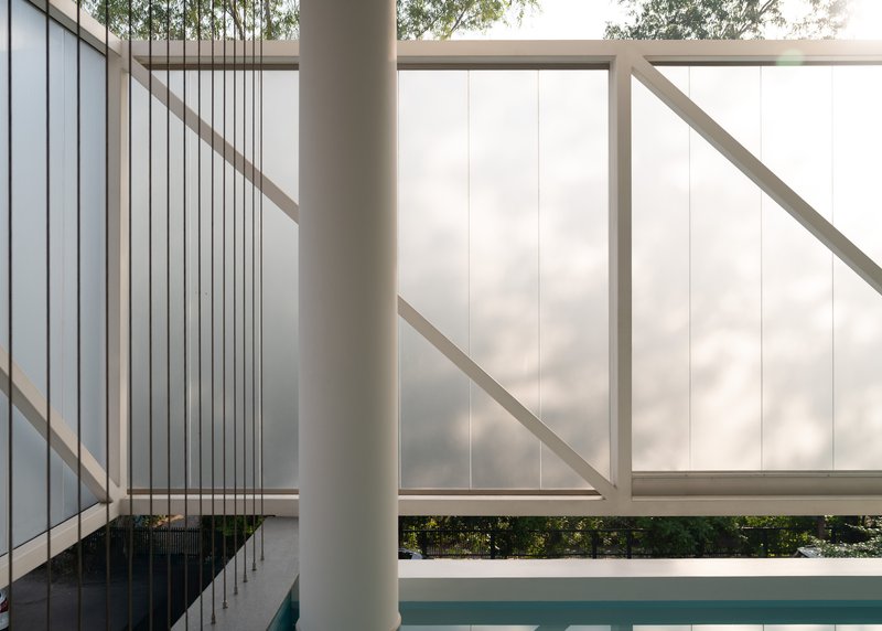 Swimming pool edge with white metal guardrails and suspended wire rods beneath a translucent screen