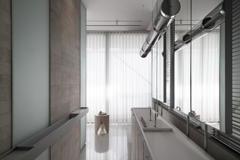 Narrow kitchen corridor with exposed ductwork and floor-to-ceiling sheer curtains filtering bright sunlight
