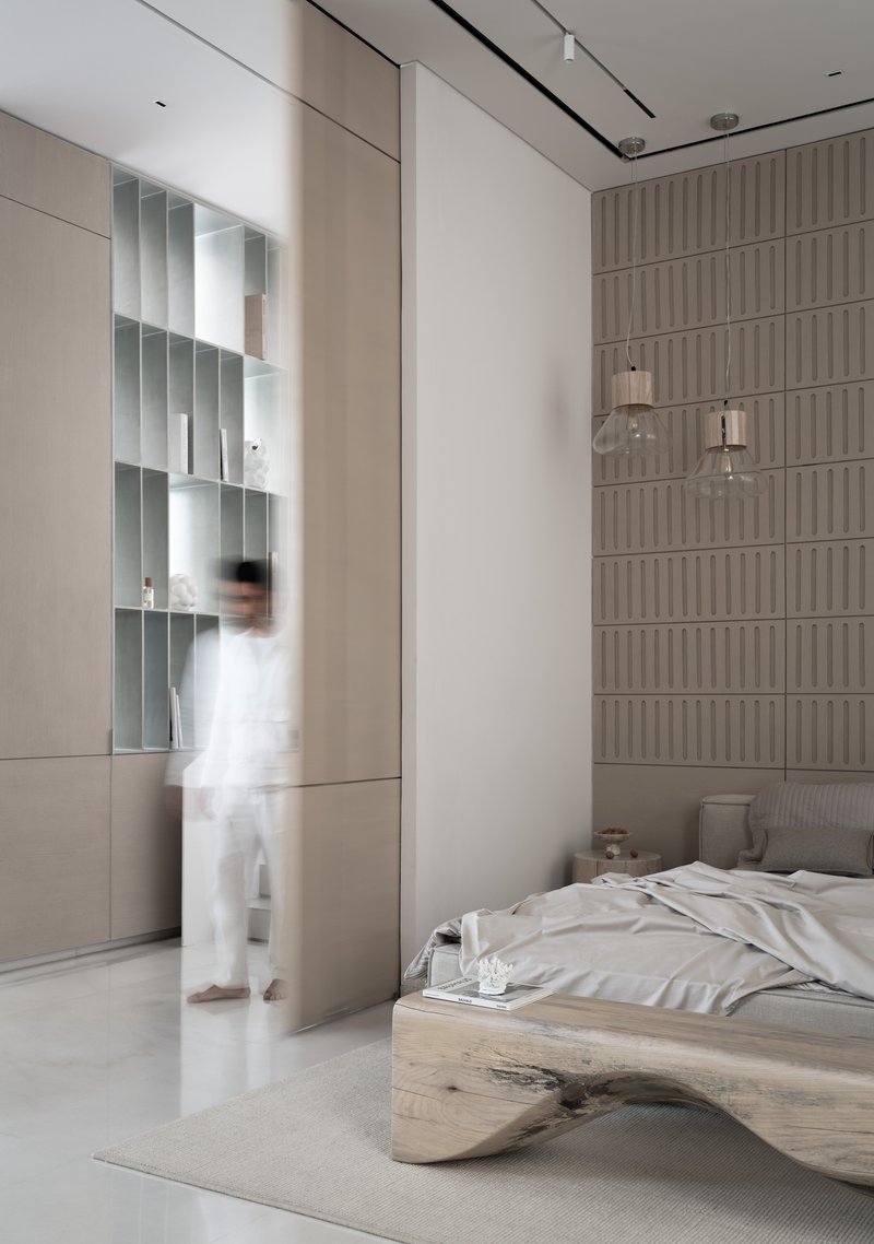 Bedroom with textured headboard wall and a blurred figure walking past mirrored alcove shelving