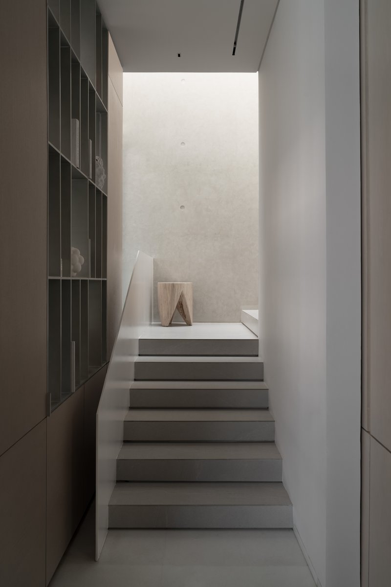 Staircase framed by dark shelving wall leading up to a landing with soft natural light