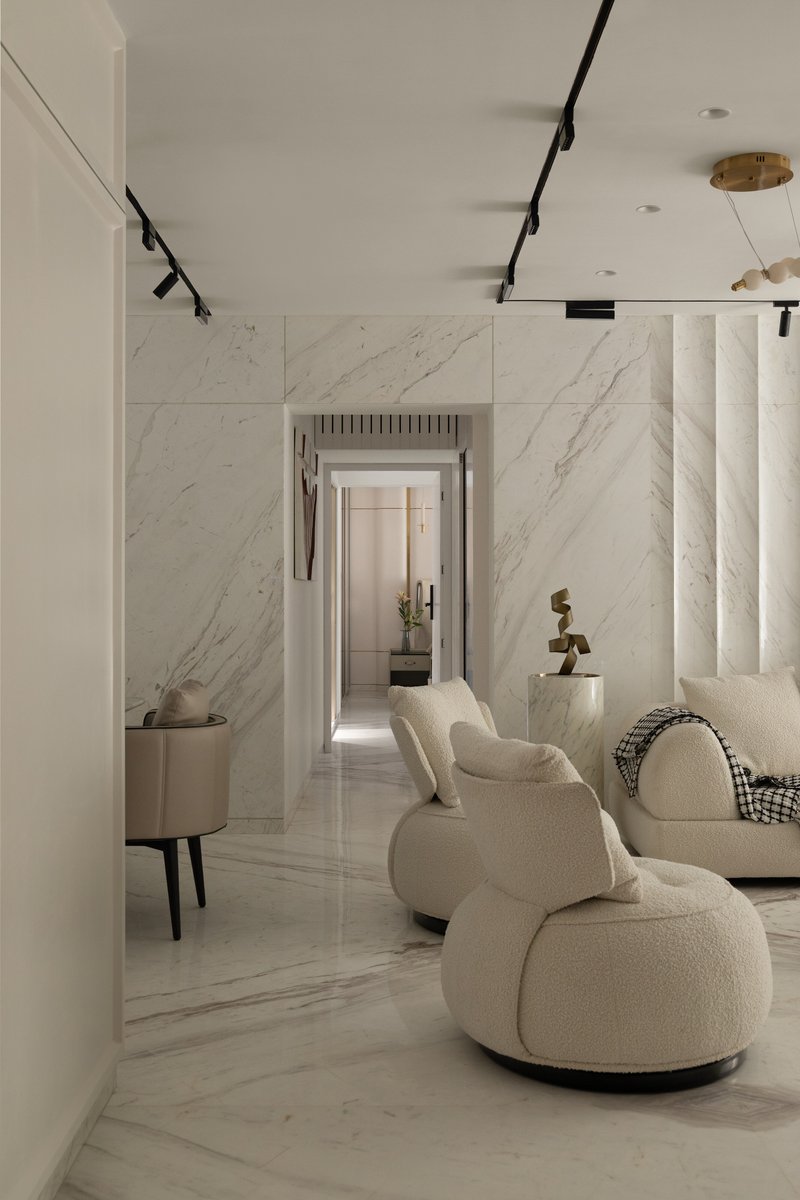 A marble-clad transitional corridor connecting the living room to the private quarters, with bouclé swivel chairs and a brass sculpture on a marble pedestal.