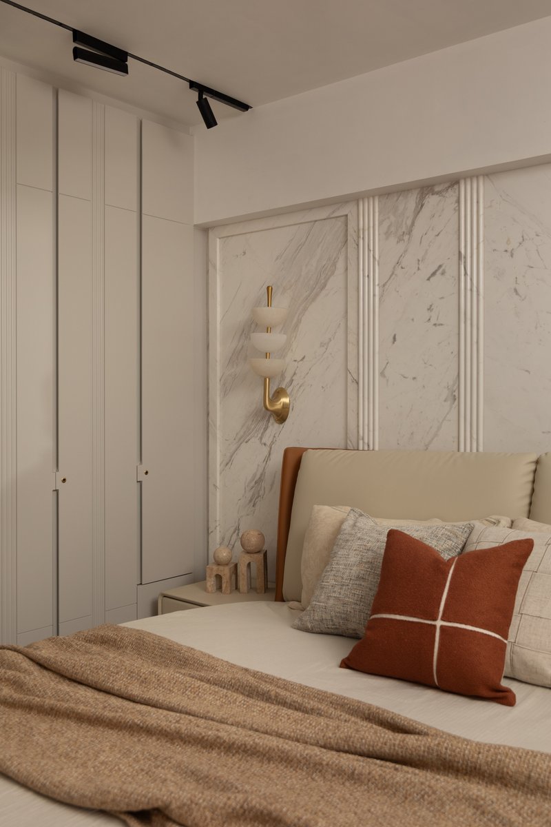 A bedroom with a book-matched marble feature wall and a brass-and-alabaster wall sconce.