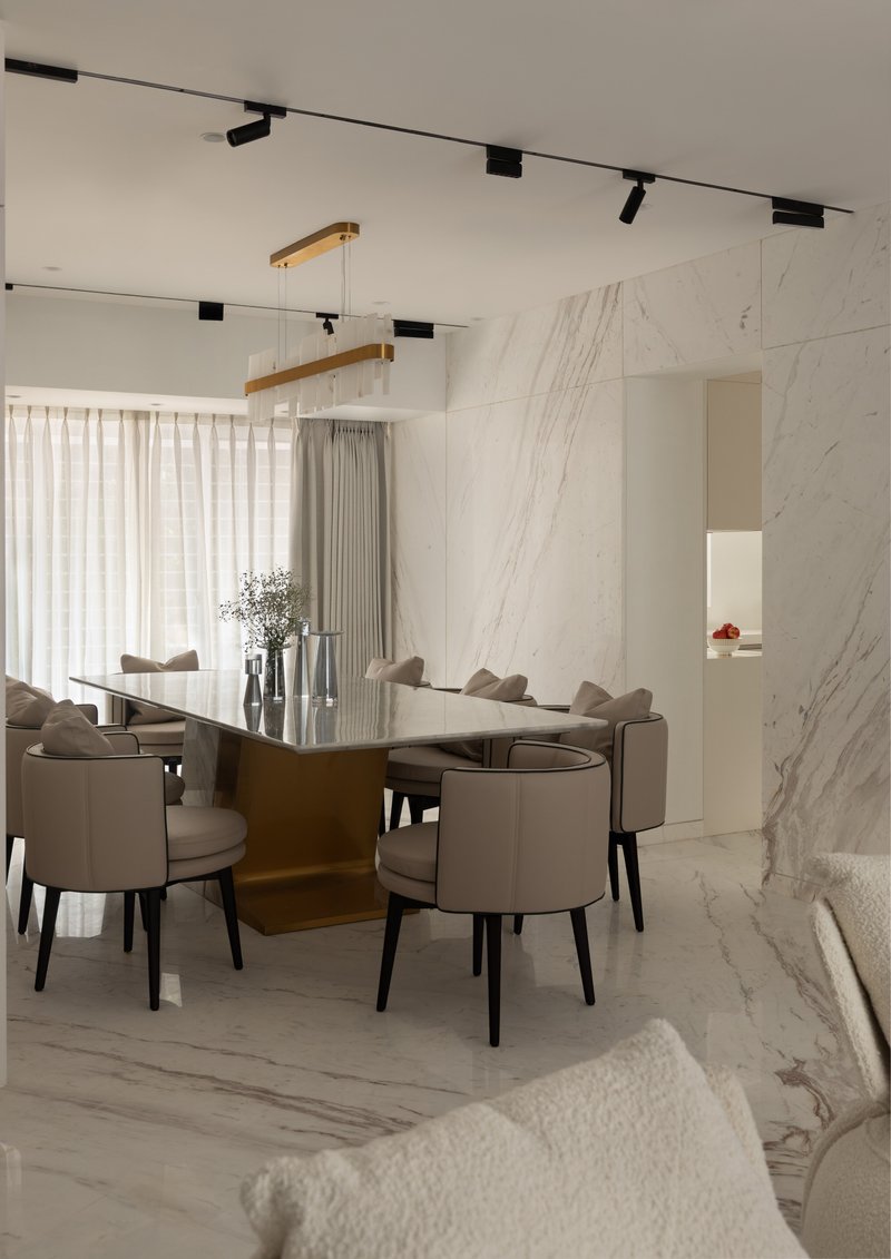 The dining table on its polished brass pedestal, against the continuous book-matched marble wall.
